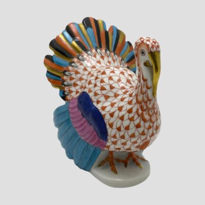 Main photo of turkey positioned diagonally across the photo with the bird facing bottom right corner and colourful tail fanned out in the top left corner. The tail is in a stripy combination of rust, turquoise, black and gold, the fishnet pattern is in rust which matches the tail nicely then the wings are in turquoise pink and blue. A quirky turkey!