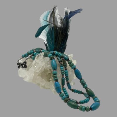 Main photo of necklace shown draped over a cluster of quartz crystal with some blue coloured feathers standing upright in the background.