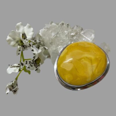 Main photo of brooch seen leaning up against a clump of quartz crystal with a sprig of white flowered orchids to the left. The size and colour of the amber is very vibrant.