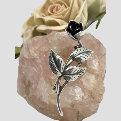 Main photo of brooch displayed on top of a rock of rose quartz with a pale pink rose in the background. The brooch is 3D in effect with the head of the rose slightly protruding from the stem and leaves.