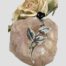 Main photo of brooch displayed on top of a rock of rose quartz with a pale pink rose in the background. The brooch is 3D in effect with the head of the rose slightly protruding from the stem and leaves.