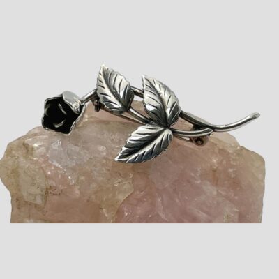 Photo of the rose brooch laid horizontally on a rock of rose quartz with the flower head on the left.