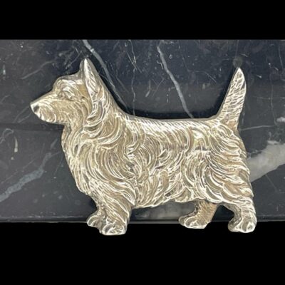 Main photo of terrier shown leaning against some black marble. The brooch is of the whole dog in profile with the head to the left facing left and the tail to the right and sticking up.
