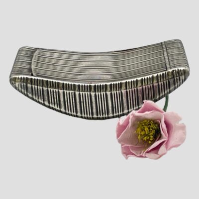 Main photo of snuff box seen from a side long angle. The curved base is visibleas well as the arch to the top. A little like a rocking boat. There is a small pink flower to the right.