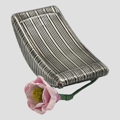 Photo of the snuff box seen from a diagonally set angle with one end lowered facing bottom right and other end upright. The small pink flower is still in the photo.