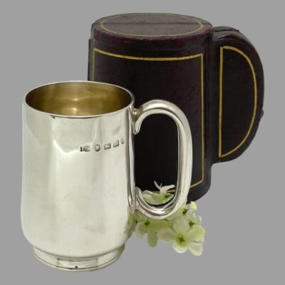 Secondary photo of the mug displayed in front of its closed case and shown in closer detail than main picture. There is a small sprig of white flowers between the mug and case..