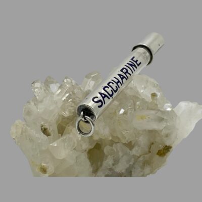 Photo of container still displayed on top of a cluster of quartz crystal and shown laid diagonally across with the ring clasp end in the foreground.