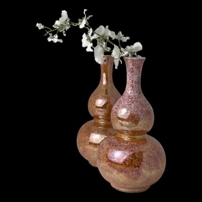 Main photo of vases displayed with one slightly behind the other. The pinker of the 2 is in the foreground to the right whilst the more orange coloured one is behind and positioned a little left of the one in front. There is a sprig of white orchids coming out of the mouth of the one on the right. The colours are very striking especially as the vases are set against a black background.