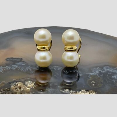 Main photo of the earrings displayed side by side on top of a slice of natural agate. Both the earrings are front facing. One pearl is above the other as in a figure of 8 with a gold band separating the 2.