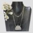 Main photo of necklace with attached purse pendant displayed on a dark wooden display stand. The chain is long and has had to be double round the neck of the display. The purse pendant is a nice size and is a very visible statement. The is a spray of small white orchids on the left shoulder of the display stand.