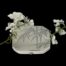 Main photo of compact laid on a flat surface against a black background. The photo is taken from a little height looking down diagonally at the bamboo decoration on the lid. The compact is propped up slightly at the back with a spray of small white orchid flowers.