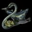 Main photo of swan shaped bowl with the front of the swan in the bottom left and the bowl back end tapering to a point in the top right corner of photo. The bowl is a triangular shape giving an impression of a swan with wings outstretched. The overall colouring is multiple shades of blue stripes in clear glass with a golden accent lower in the bowl. The is a small posy of pale green/blue roses on the base of the neck.