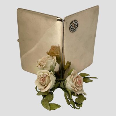 Main photo of case shown open and displayed upright. Both external sides of the case are on display with the MGM logo disc on the right side but centre top in this photo. There is a small posy of pale pink roses in the centre foreground - gives a real Hollywood look!