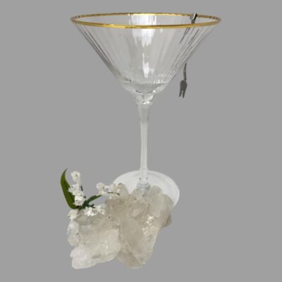 Photo of one fork shown hanging on the outside of the cocktail glass. There is a lump of quartz crystal in the foreground with some small white flowers on top.