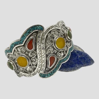 Main photo of the bangle leaning against a small rock of lapis lazuli. The darker blue of the lapis enhances the mosaic turquoise, other semi precious stones and the intricate work on the silver.