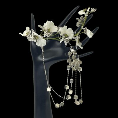 Main photo of necklace displayed draped on a dark coloured display hand with the majority of the cubes hanging on the right. There is a small spray of white orchids across the fingers to the top.