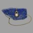 Main photo of necklace with pendant displayed hanging off the side of a rock of natural lapis lazuli, the blue of the lapis enhances the pearl and gold. The chain goes down the back of the lapis rock and reappears out front in a circular pattern with the end disappearing behind the rock.