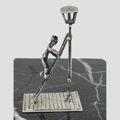Photo of miniature seen from a side view with lamp to the right and lamplighter mid climb halfway up ladder.