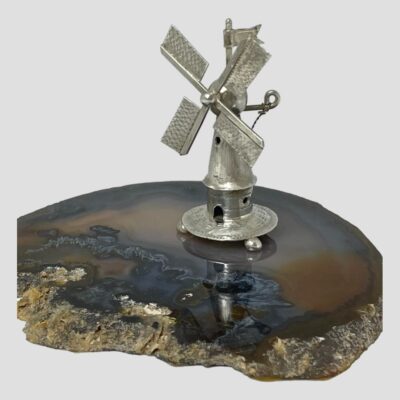 Main photo of windmill shown displayed on top of a slice of brown agate. The windmill frontage is facing towards the bottom left of photo. The windmill stands on 3 small ball feet.