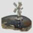 Main photo of windmill shown displayed on top of a slice of brown agate. The windmill frontage is facing towards the bottom left of photo. The windmill stands on 3 small ball feet.