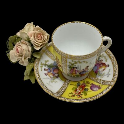 Photo Of cup on the saucer and seen from a slight height looking down. The handle is to the right and the posy of pink roses is to the left.