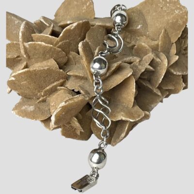 Main photo of bracelet displayed laid across a rock of desert sand rose with one end in the centre foreground. The alternating ball & cage twist links are very striking and eye catching.
