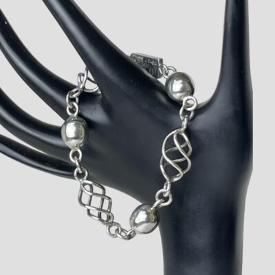 Photo of bracelet displayed on a black display stand with the bracelet hooked around the index finger of the hand. The bracelet has the clasp closed so is displayed in a circular form.