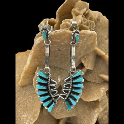 Close up photo of the errings shown forward facing and still hanging from a rock of desert sand rose. The sand colour of the rock and the black background enhances the earrings colours.