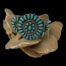 Main photo of bracelet displayed on top of a rock of desert sand rose with the front facing forward. There is a large circle to the centre with a frame of needlepoint turquoise all facing inward, a gap of silver with rope like pattern, then another circle of round turquoise stones with an oval to the centre. The centre circle is flanked to either side by a semi circle of 7 needlepoint turquoise stones. The open end of the semi circles are attached to the central circle.