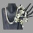Main photo showing the necklace displayed on a dark wood bust and the bracelet hanging from the fingers of a dark hand display stand. The necklace is shown forward facing and then bracelet is seen width ways. There is a spray of small white orchids between the 2 stands.
