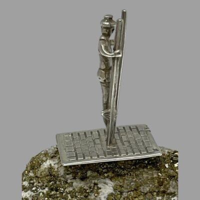 Main photo of stilt walker shown in profile facing direct to the right. The miniature is on top of a small natural rock. The stilts are not high ones with the standing ledge low to the ground so the walker is holding the top of the stilts.