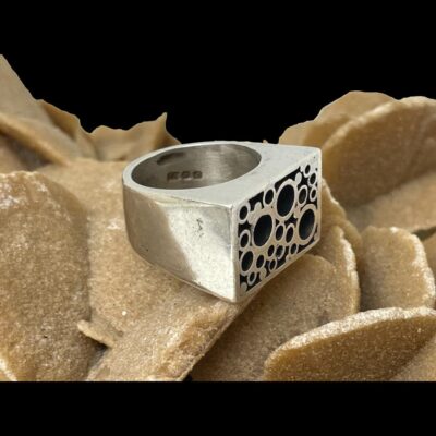 Photo of ring displayed on top of a rock of desert sand rose and shown with ring front facing towards the bottom right. The ring is fairly uniform in thickness throughout and is a fine lump of modernist-brutalist jewellery.