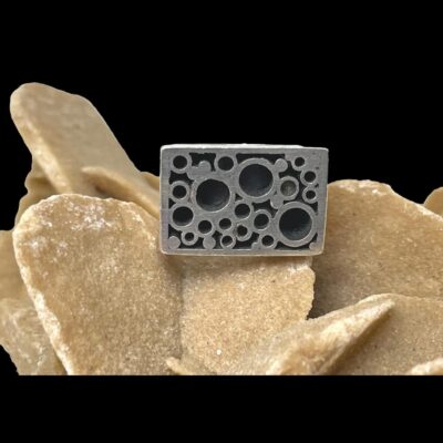 Main photo of ring displayed on top of a rock of desert sand rose and shown with the ring front forward facing. The bubbles are black in colour and are actually sunken in. Looks a little like something off a car or other mechanical metal especially since the silver is matt not polished.