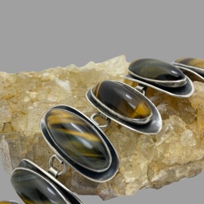 Close up photo of a few of the panels on the bracelet shown still laid across a rock of natural sandy coloured quartz crystal. It is clearly visible that the tigers eye cabochons are raised off of their convex lower panels. Almost gives an impression of mussels on a rock.