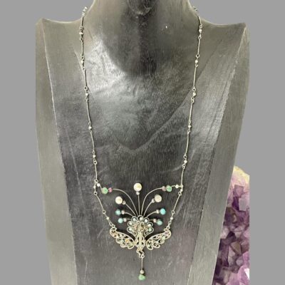 Main photo of necklace shown displayed on a dark wood display stand with the necklace front forward facing. The chain is generous in length so the pendant area is quite low on the display stand. There is a lump of natural amethyst behind the display stand.