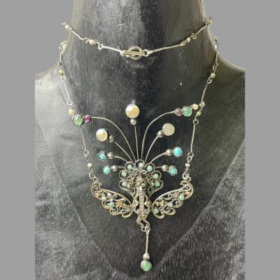 Photo of necklace shown displayed on a dark wood display stand with the chain doubled up around the neck and the clasp area shown above the peacock.