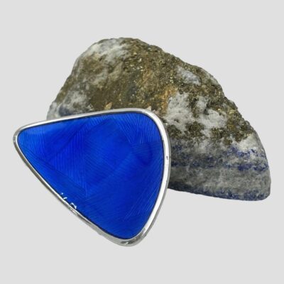 Secondary photo of brooch shown leaning against the not blue side of the lapis rock and shown from a side view with the brooch front facing towards the left and up. There is what appears to be some white coloured specks at the centre bottom but this is light reflection only. The enamel is in perfect condition.