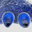 Main photo of earrings displayed in front of a piece of natural smooth rock of blue lapis lazuli rock with the earring fronts forward facing. The blue enamel on the earrings are of a more vibrant colour and stand out well against the blue of the lapis. The shape of the earring front is like a parachute with a concave dip in the middle and framed within a sterling silver border.
