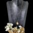 Main photo of necklace displayed on a dark wood display stand and seen forward facing. The chain is generous in length so the petite sized locket hangs quite low down the display stand. There is a rock of desert sand rose with white orchid flowers at the base foreground of the stand.