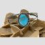 Main photo of cuff bracelet displaed on top of a rock of natural desert sand rose with the cuff front and turquoise forward facing. The turquoise is set on a frame of sterling silver with the frame of the cuff in 3 lines 2 smooth silver to the top and bottom and a twist line through the centre. The silver frame around the turquoise has short lines to the north, east, south and west of the turquoise representing the 4 winds perhaps.