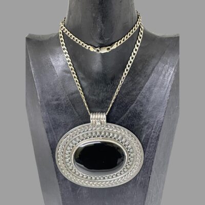 Main photo of necklace displayed on a dark wooden display stand and seen with the pendant front forward facing. The chain has had to be doubled up as it is quite long so the clasp is visible at the centre of the neck. The pendant is immense and is almost as wide as the display stand. If you are after a statement piece like no other, this has to be the one!