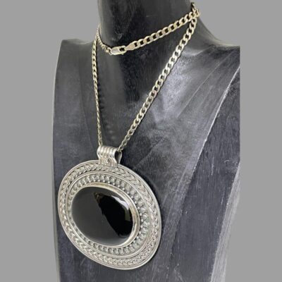 Photo of necl;ace displayed on a dark wooden stand with the pendant front facing towards the bottom left corner of photo.