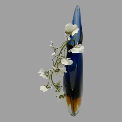Photo of vase seen from the slender side angle. The higher side of lip is in the background. The spray of white orchids are hanging down the left side.