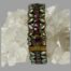 Main photo of bracelet shown vertically upright with a rock of natural quartz crystal through the middle holding it up. The centre row of the bracelet houses the dark pink stones with clear glass circles and petals on either side. Each area with a glass stone piece is enhanced with an outer painted frame of bright green enamel which along with the gilt, makes this bracelet truly stand out.