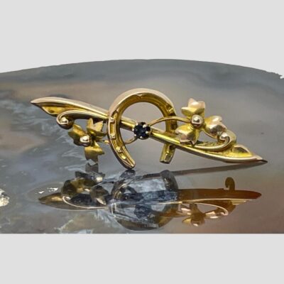 Main photo of brooch displayed on top of a slice of natural agate with the brooch front forward facing. The horseshoe is open end down as it should be and the single sapphire is to the centre. (Better described in photo 2)
