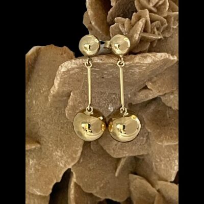 Main photo of the earrings displayed side by side vertically on a cluster of desert sand rose. The small ball sits at the end of the earring posts with a short bar attached and large ball at the end of the bar. They are simple but very elegant earrings.