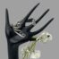 Main photo of bracelet displayed on a black display hand with the bracelet positioned around the forefinger. The curled prong ends of the fork are to the left. There is additionally a small spray of white orchids hanging off the little finger.