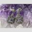 Main photo of earrings displayed side by side and hanging from a rock of natural amethyst. The top area with posts attached are like a half hoop but wider at top finishing almost in a point at bottom which curves backwards like a hook. Attached to this upper piece is a square of silver with marcasite and a square cut amethyst to the centre. Petal shapes extend from the 4 corners of the central square like a flower.