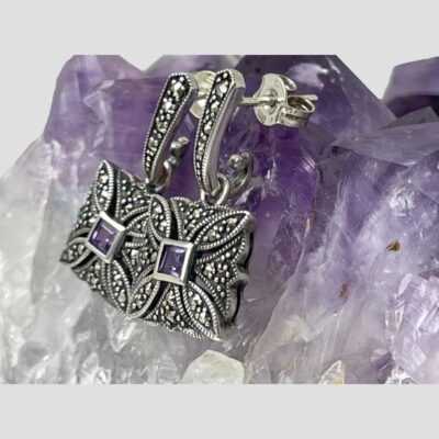 Photo of earrings still displayed on a rock of amethyst and seen from a side angle with the earring fronts facing left.