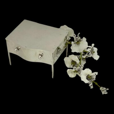 Photo of jewellery box still shown closed but from a raised angle looking down at the top. The frontage is still visible and the spray of white orchids is still to the right.